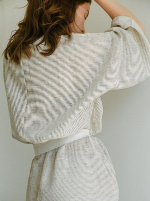 woman facing backwards in pinstripe linen robe with white tie belt around her waist