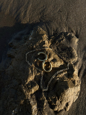 gold hoop earrings and gold chain necklace on the rock by the shore