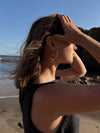 woman wearing gold hoop earring and black tank top standing by the shore
