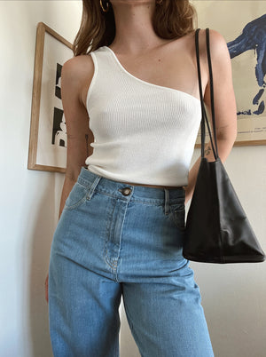 woman in white aymmetric knit top and light blue denim pants carrying a black leather tote