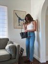 woman in white aymmetric knit top and light blue denim pants carrying a black leather shoulder bag