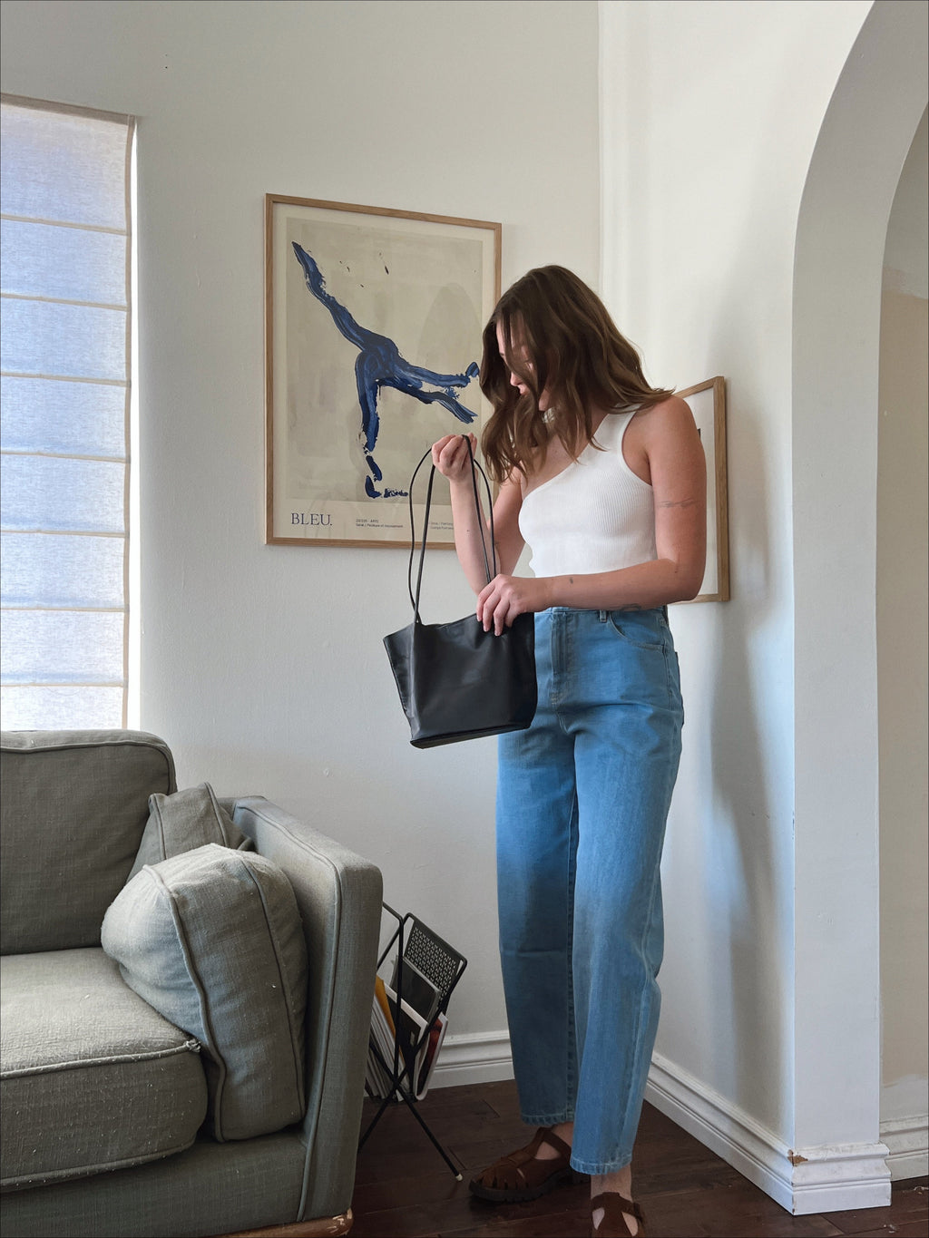 woman in white aymmetric knit top and light blue denim pants carrying a black leather shoulder bag